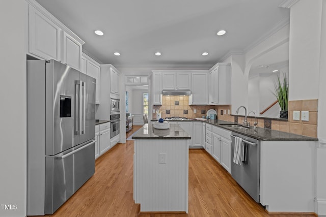 kitchen with stainless steel appliances, a center island, a sink, under cabinet range hood, and ornamental molding