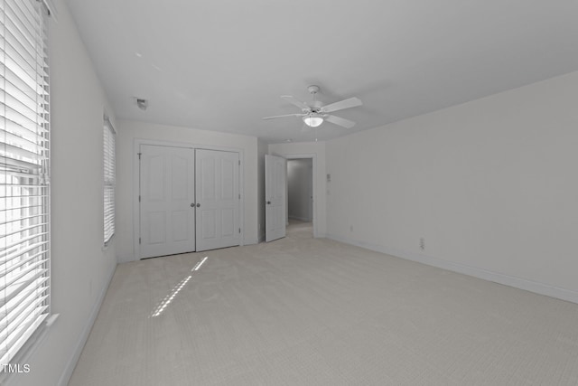unfurnished bedroom featuring baseboards, light carpet, multiple windows, and a closet