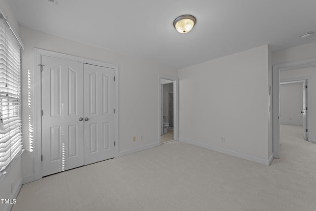 unfurnished bedroom with light carpet, a closet, and baseboards