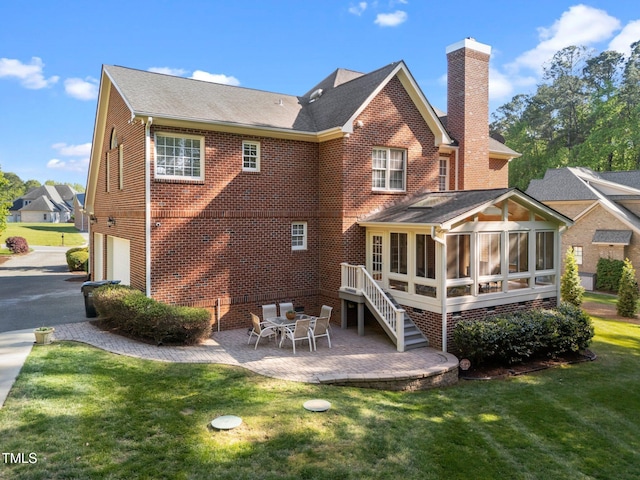 back of property with a chimney, an attached garage, a yard, a patio, and a sunroom
