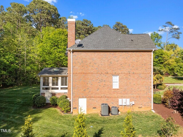 view of home's exterior featuring a chimney, crawl space, brick siding, a lawn, and a sunroom