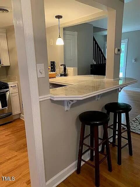 bar with light wood-type flooring, pendant lighting, stairs, and stove