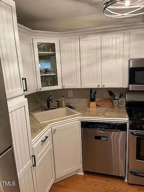 kitchen with white cabinetry, stainless steel appliances, light countertops, and a sink