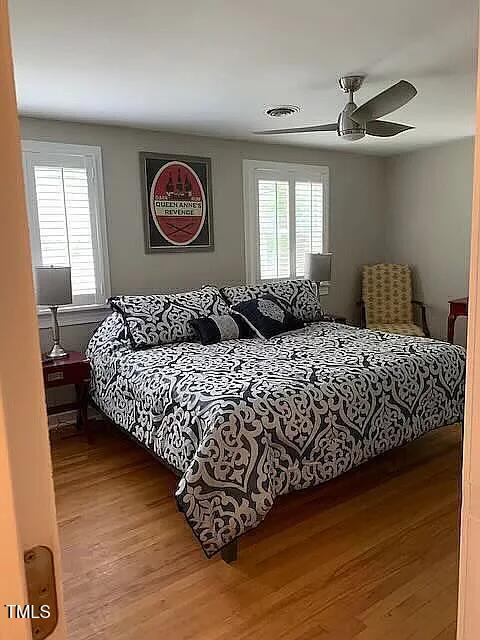bedroom with a ceiling fan, wood finished floors, and visible vents