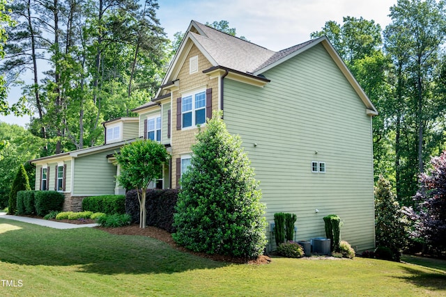 view of side of property featuring a lawn, a shingled roof, and central AC