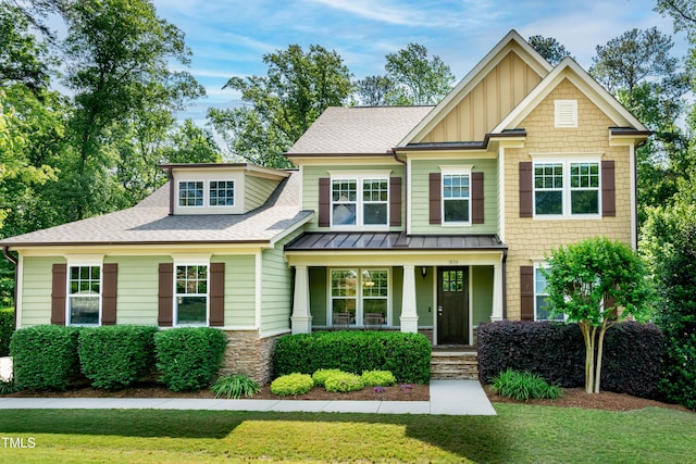 craftsman-style house featuring board and batten siding, roof with shingles, a front lawn, and covered porch