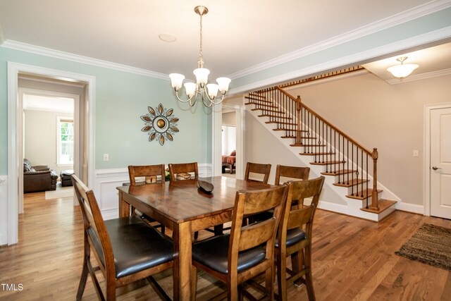 dining space with an inviting chandelier, a wainscoted wall, stairs, light wood-type flooring, and ornamental molding