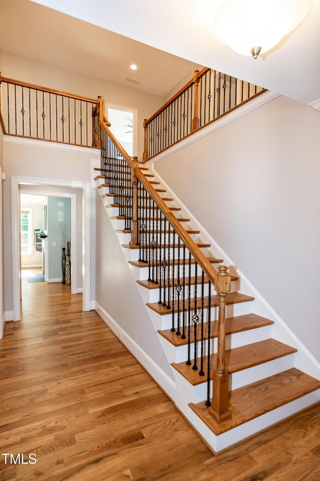 stairs featuring baseboards, recessed lighting, a high ceiling, and wood finished floors