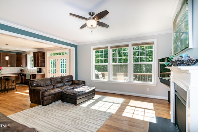 living room with a ceiling fan, plenty of natural light, ornamental molding, and light wood finished floors