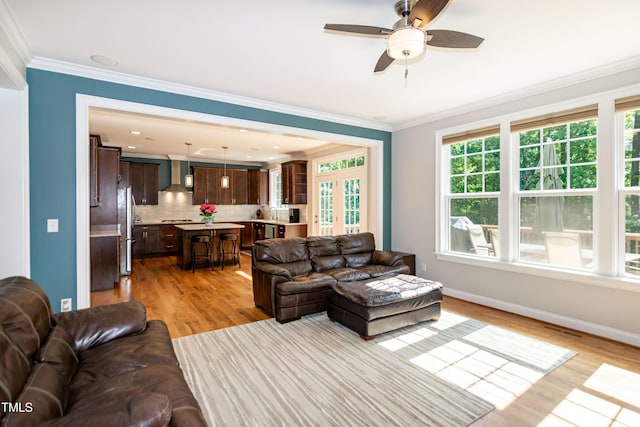 living area featuring light wood-type flooring, ornamental molding, baseboards, and ceiling fan