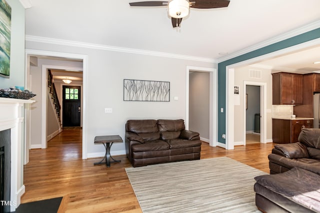 living room featuring crown molding, a fireplace, a ceiling fan, light wood-type flooring, and visible vents