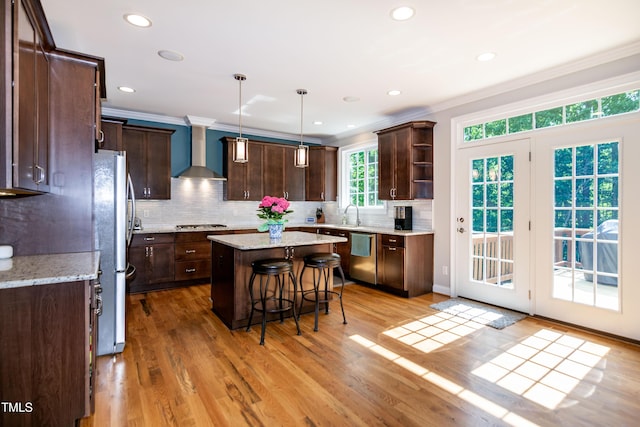 kitchen featuring wall chimney range hood, dark brown cabinetry, a breakfast bar, stainless steel appliances, and ornamental molding