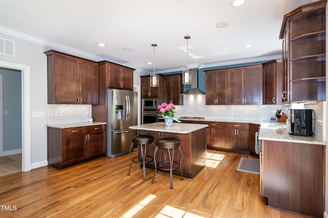 kitchen featuring a breakfast bar area, wall chimney exhaust hood, stainless steel appliances, a kitchen island, and ornamental molding