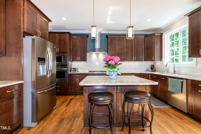 kitchen with a center island, a sink, ornamental molding, stainless steel appliances, and wall chimney exhaust hood