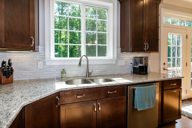 kitchen featuring stainless steel dishwasher, a sink, decorative backsplash, and light stone counters
