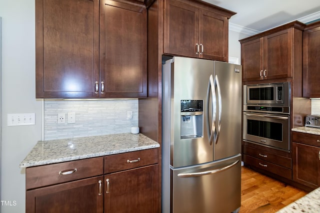kitchen featuring light stone counters, light wood-type flooring, backsplash, and stainless steel appliances