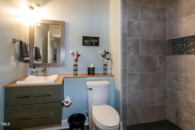 full bathroom with toilet, a tile shower, and vanity