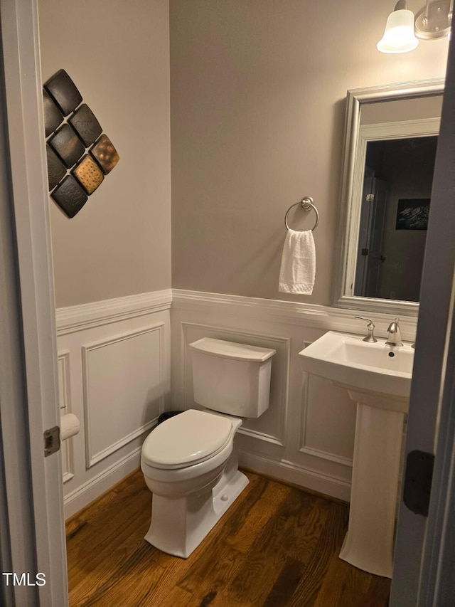 half bath with toilet, wainscoting, wood finished floors, and a decorative wall