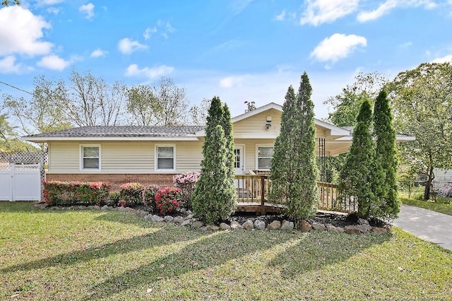 ranch-style house featuring brick siding, a front lawn, fence, and a deck