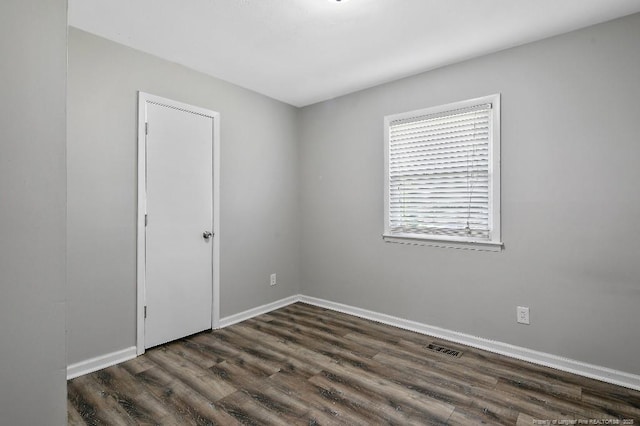 spare room with baseboards, dark wood-type flooring, and visible vents
