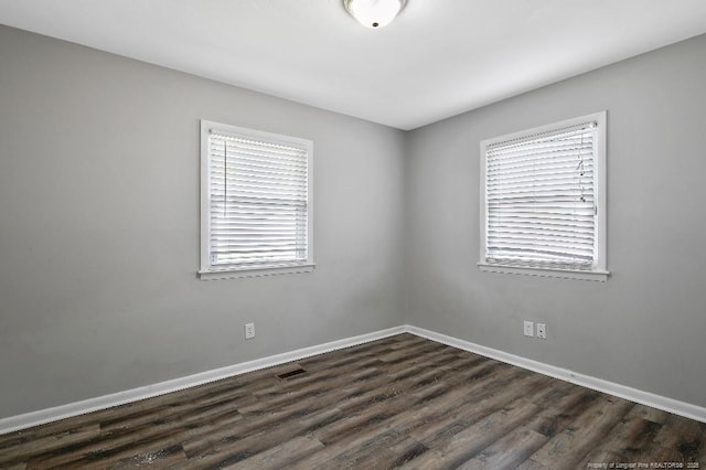 empty room featuring dark wood-type flooring, visible vents, and baseboards