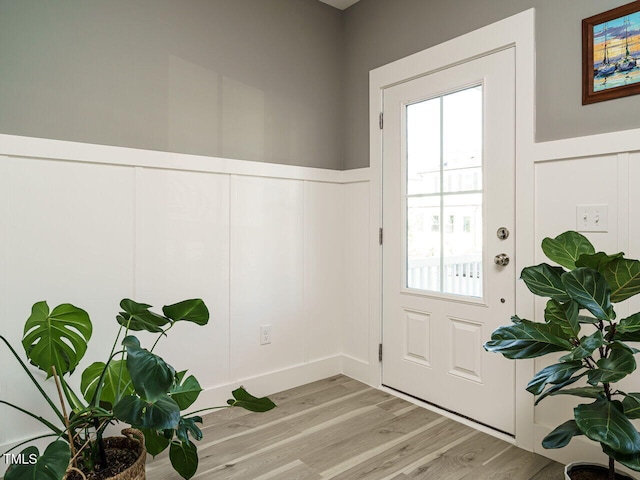 doorway to outside featuring light wood finished floors, a wealth of natural light, and a decorative wall