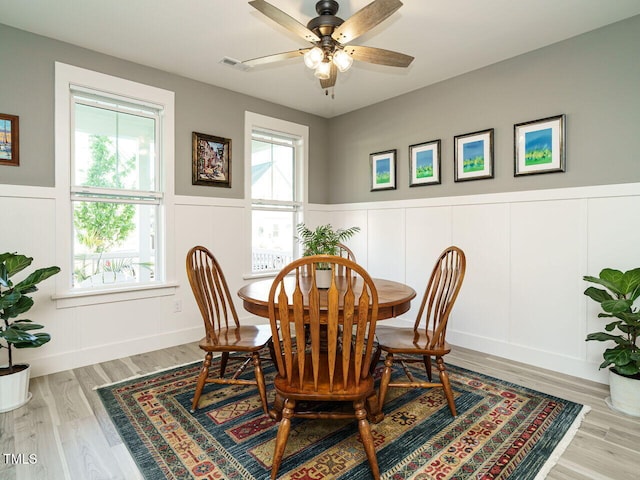 dining area featuring wood finished floors, a decorative wall, a ceiling fan, and wainscoting