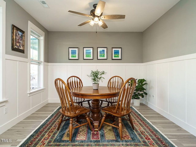 dining room with light wood finished floors, a wainscoted wall, visible vents, a decorative wall, and ceiling fan