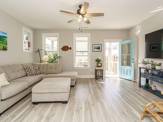 living area featuring baseboards, light wood-style flooring, ceiling fan, and plenty of natural light