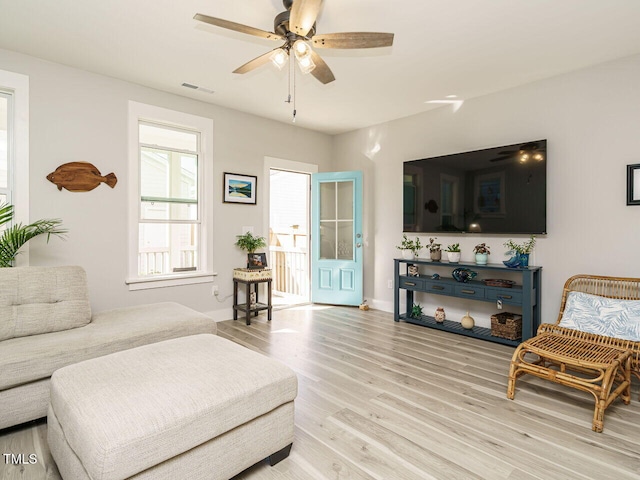 living room with light wood-style flooring, visible vents, a ceiling fan, and baseboards