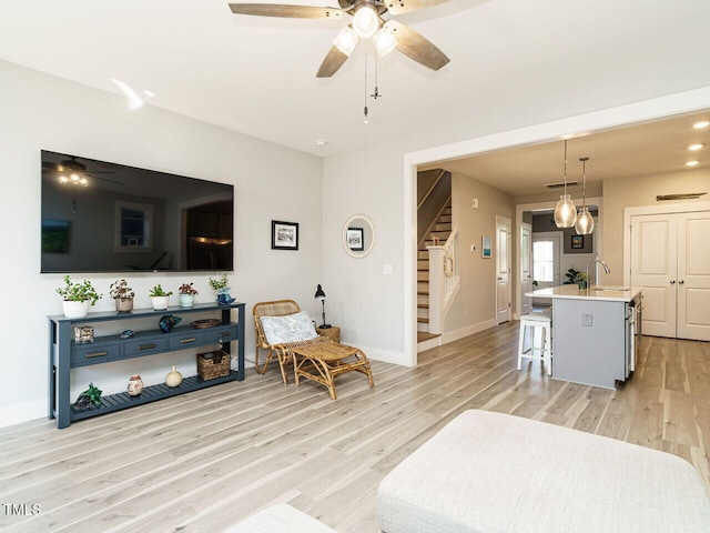 living room with light wood finished floors, stairway, a ceiling fan, and baseboards