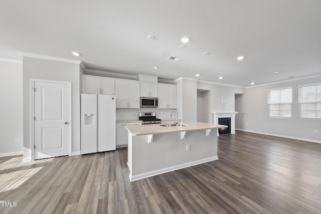 kitchen featuring a sink, a center island with sink, crown molding, light countertops, and appliances with stainless steel finishes