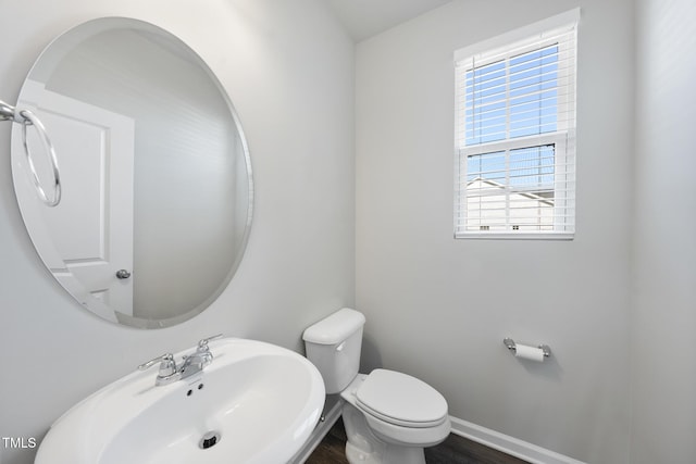 half bathroom with toilet, baseboards, and a sink