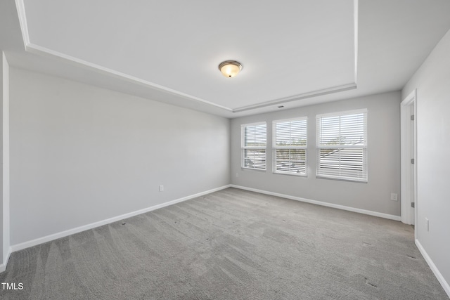 unfurnished room with carpet floors, a tray ceiling, and baseboards
