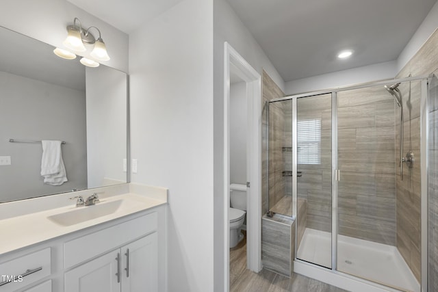 bathroom with toilet, wood finished floors, vanity, and a stall shower