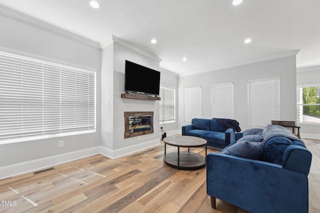 living area with a glass covered fireplace, baseboards, ornamental molding, visible vents, and recessed lighting