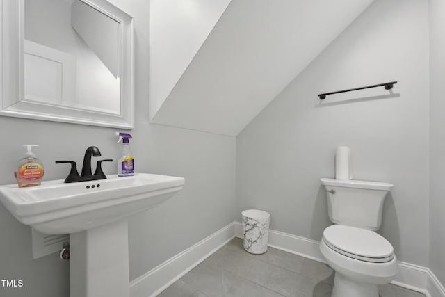 half bath with lofted ceiling, toilet, and baseboards