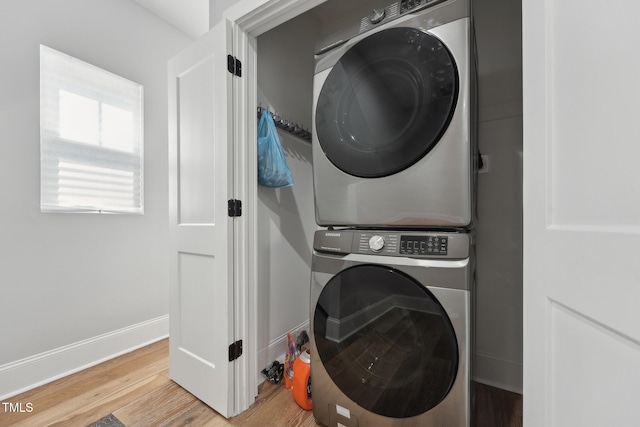 washroom featuring baseboards, stacked washer / drying machine, wood finished floors, and laundry area