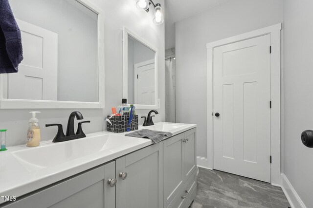 bathroom with double vanity, marble finish floor, baseboards, and a sink