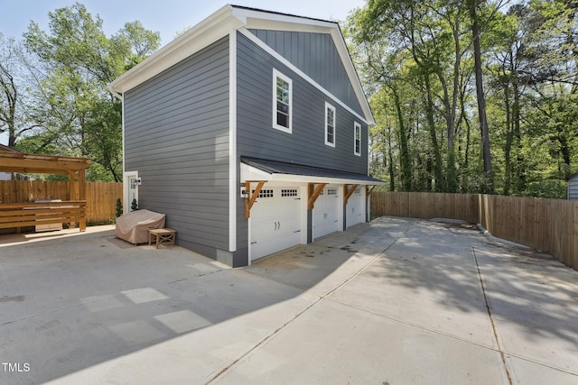 view of side of property featuring concrete driveway, an attached garage, fence, and board and batten siding
