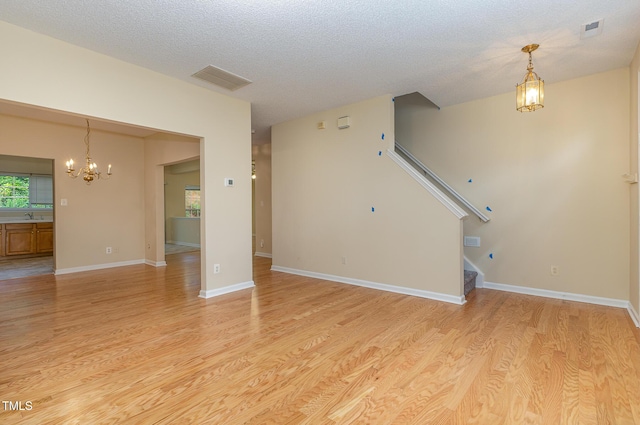 1031 Lake Moraine Pl, Raleigh, NC 27607 - unfurnished living room with a chandelier, light wood-style flooring, stairs, a sink, and a textured ceiling
