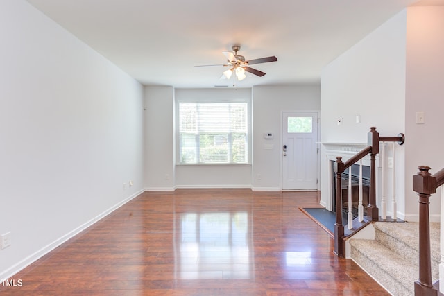 unfurnished living room featuring baseboards, a ceiling fan, stairs, and wood finished floors