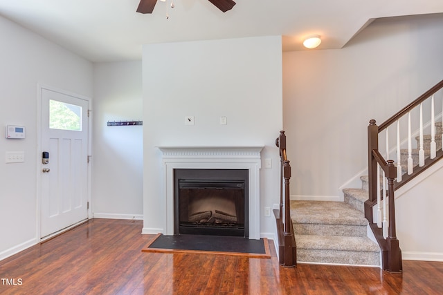 unfurnished living room with a ceiling fan, wood finished floors, baseboards, a fireplace with raised hearth, and stairs