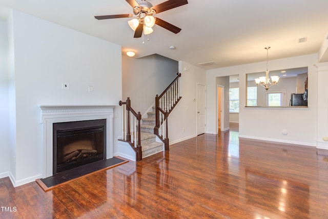 unfurnished living room with stairs, wood finished floors, baseboards, a fireplace with raised hearth, and ceiling fan with notable chandelier