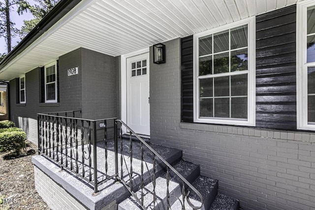 doorway to property with covered porch and brick siding