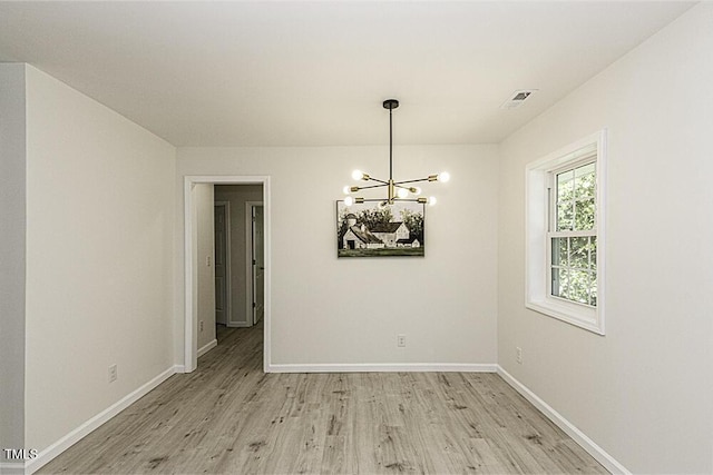 unfurnished dining area with light wood finished floors, visible vents, a notable chandelier, and baseboards