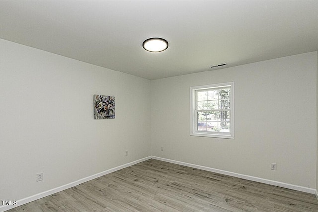 spare room with light wood finished floors, visible vents, and baseboards