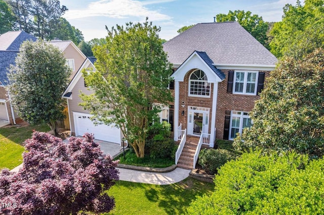 colonial home with a garage, brick siding, and roof with shingles
