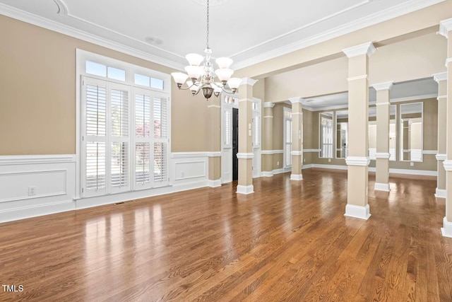unfurnished dining area featuring an inviting chandelier, a decorative wall, crown molding, and decorative columns