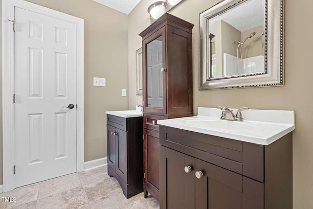 bathroom featuring a sink, two vanities, baseboards, walk in shower, and a textured ceiling